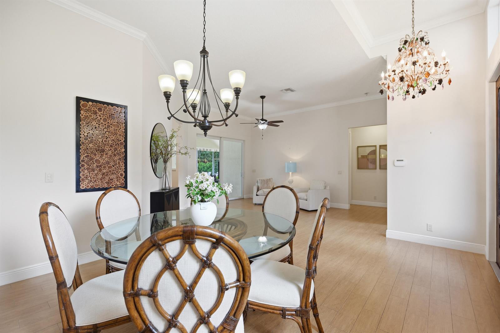 A dining area with a glass table and rattan chairs sits beneath a chandelier — 17593 Winterhawk, Jupiter FL 33478, JUPITER, FL