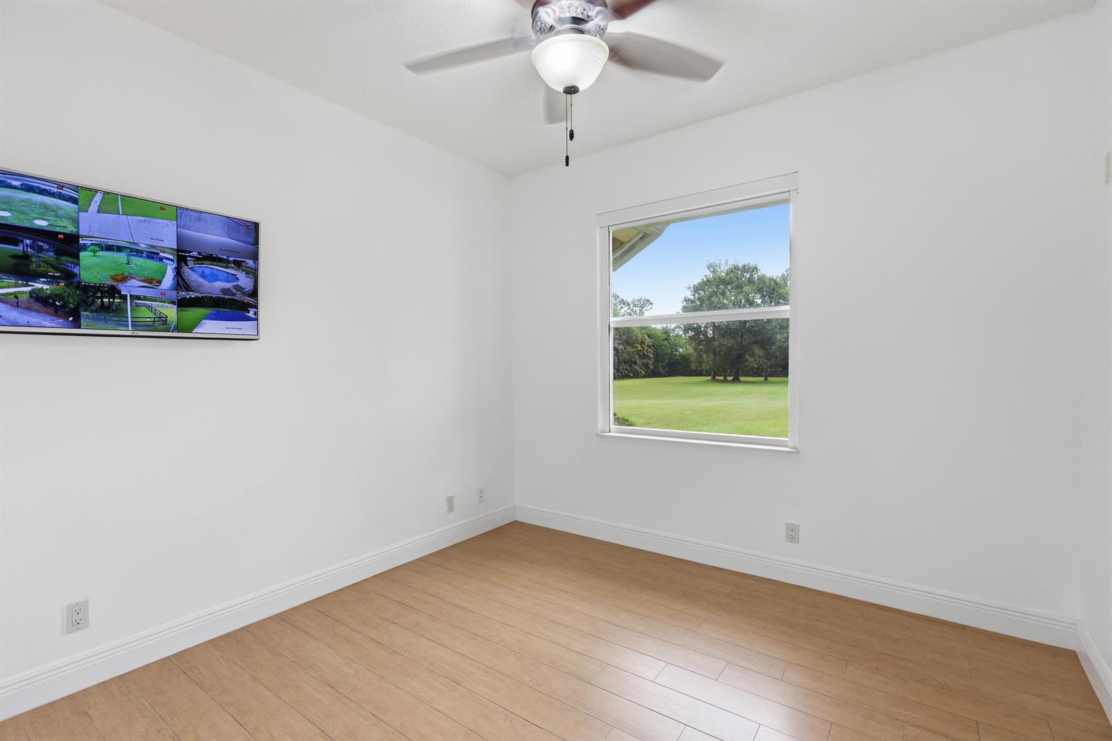 An empty room with light wood flooring, white walls, a ceiling fan, and a wall-mounted monitor — 17593 Winterhawk, Jupiter FL 33478, JUPITER, FL