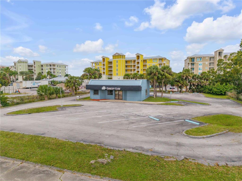 A small, blue, single-story comedy club building sits in the center of a paved parking lot — 109 N CAUSEWAY, NEW SMYRNA BEACH, FL