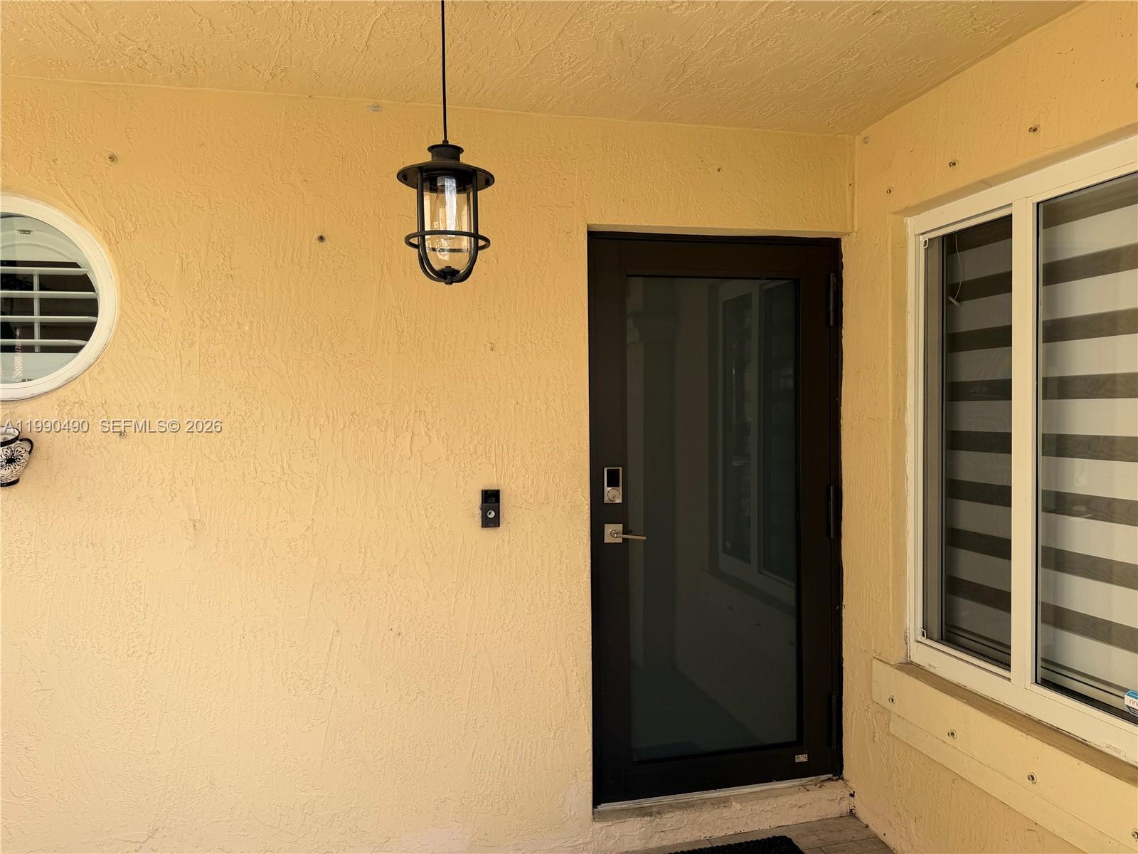 A yellow stucco exterior wall features a dark door, a hanging lantern, and a window — 7431 SW 163rd Pl, Miami FL 33193, MIAMI, FL