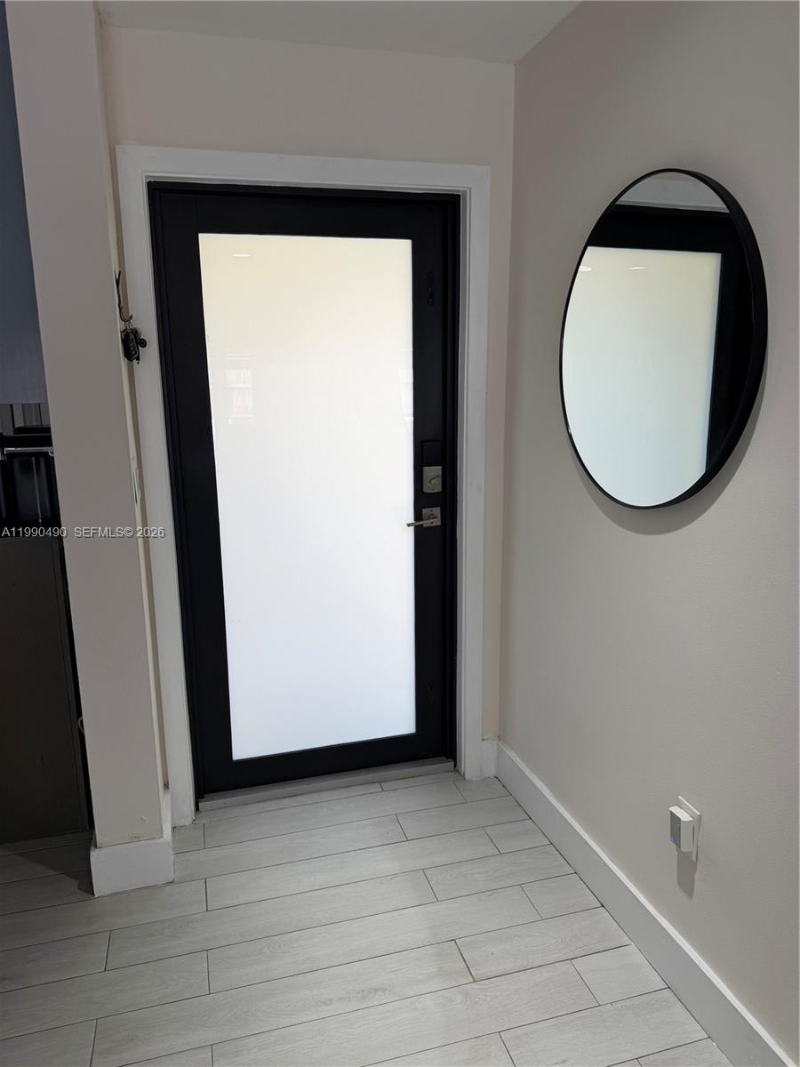 An entryway features a black-framed glass door, a round wall mirror, and light-colored tile flooring — 7431 SW 163rd Pl, Miami FL 33193, MIAMI, FL