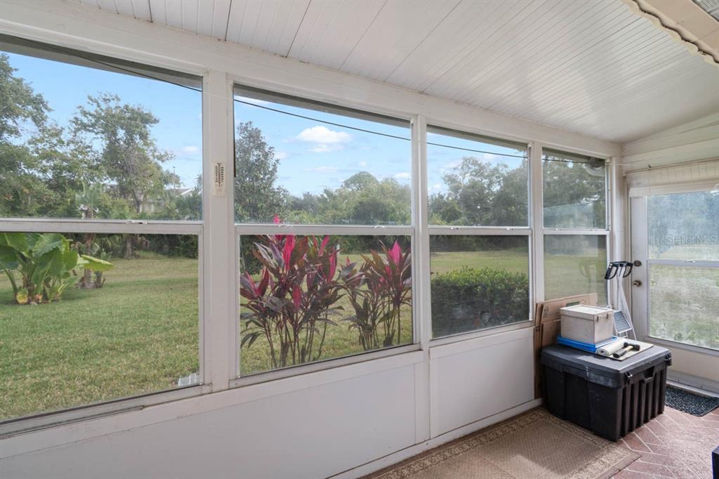 A sunroom with large windows overlooking a grassy backyard and tropical plants — 1802 BEDFORD LANE UNIT 2, SUN CITY CENTER, FL