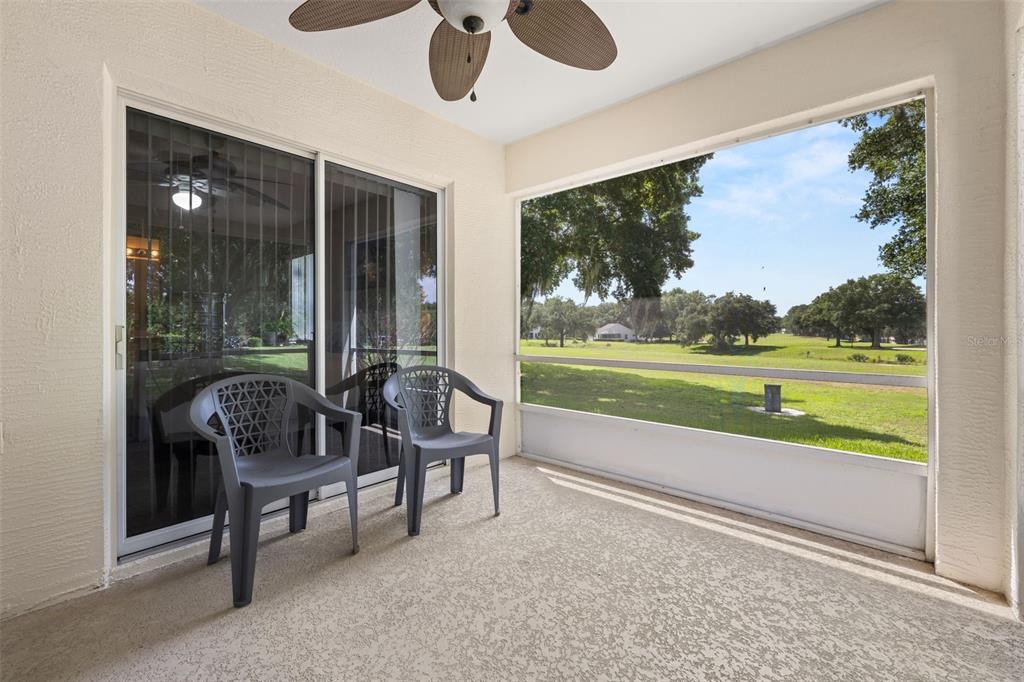 A screened-in patio features two gray plastic chairs, a ceiling fan, and a golf course view — 3604 KINGSWOOD COURT, CLERMONT, FL