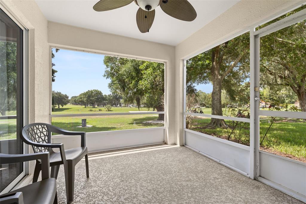 A screened-in porch with a textured floor, ceiling fan, and views of a golf course — 3604 KINGSWOOD COURT, CLERMONT, FL