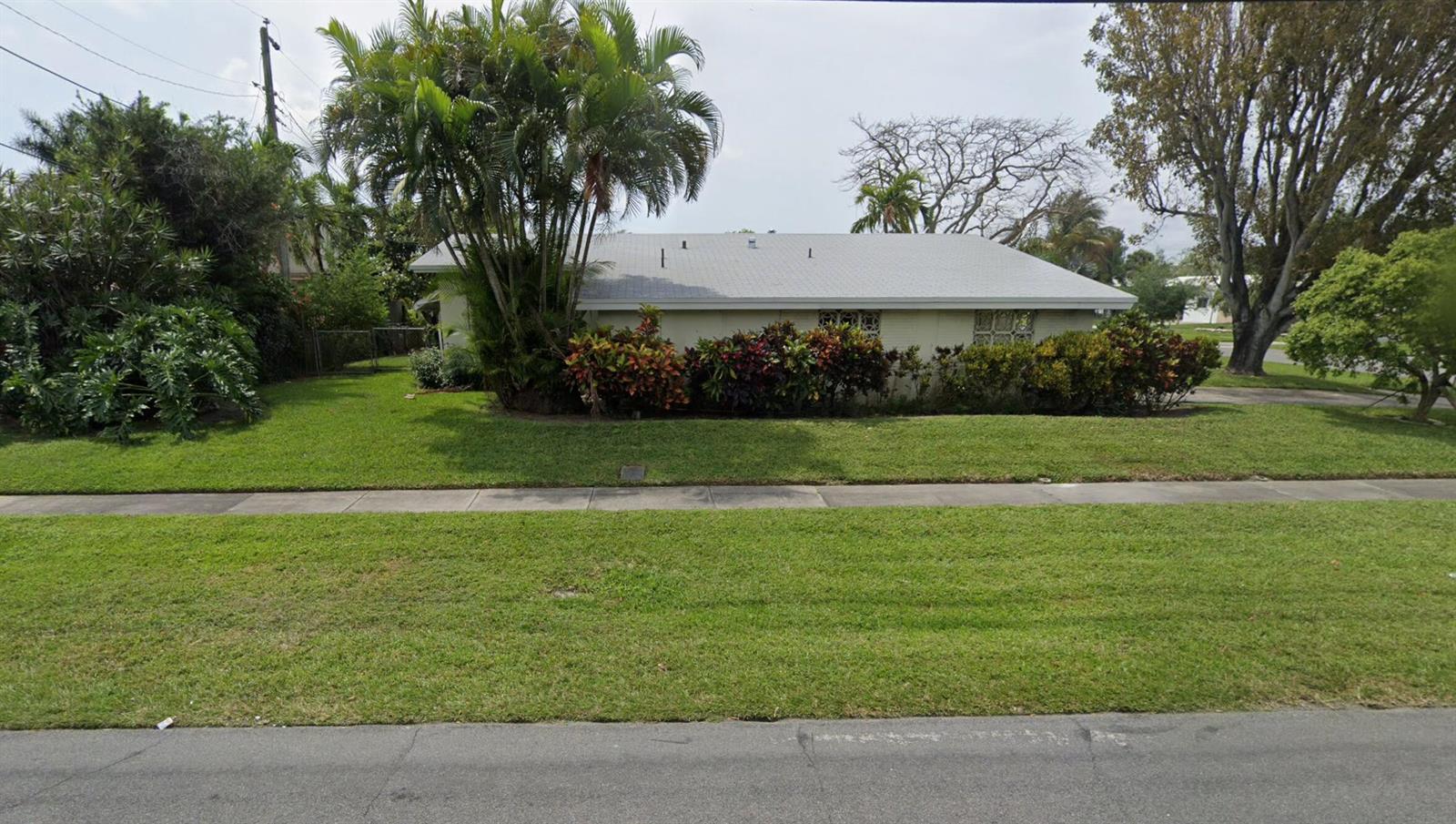 A single-story house with a light-colored exterior, a gray roof, and lush landscaping — 712 NE 23rd Terrace, Pompano Beach FL 33062, POMPANO BEACH, FL
