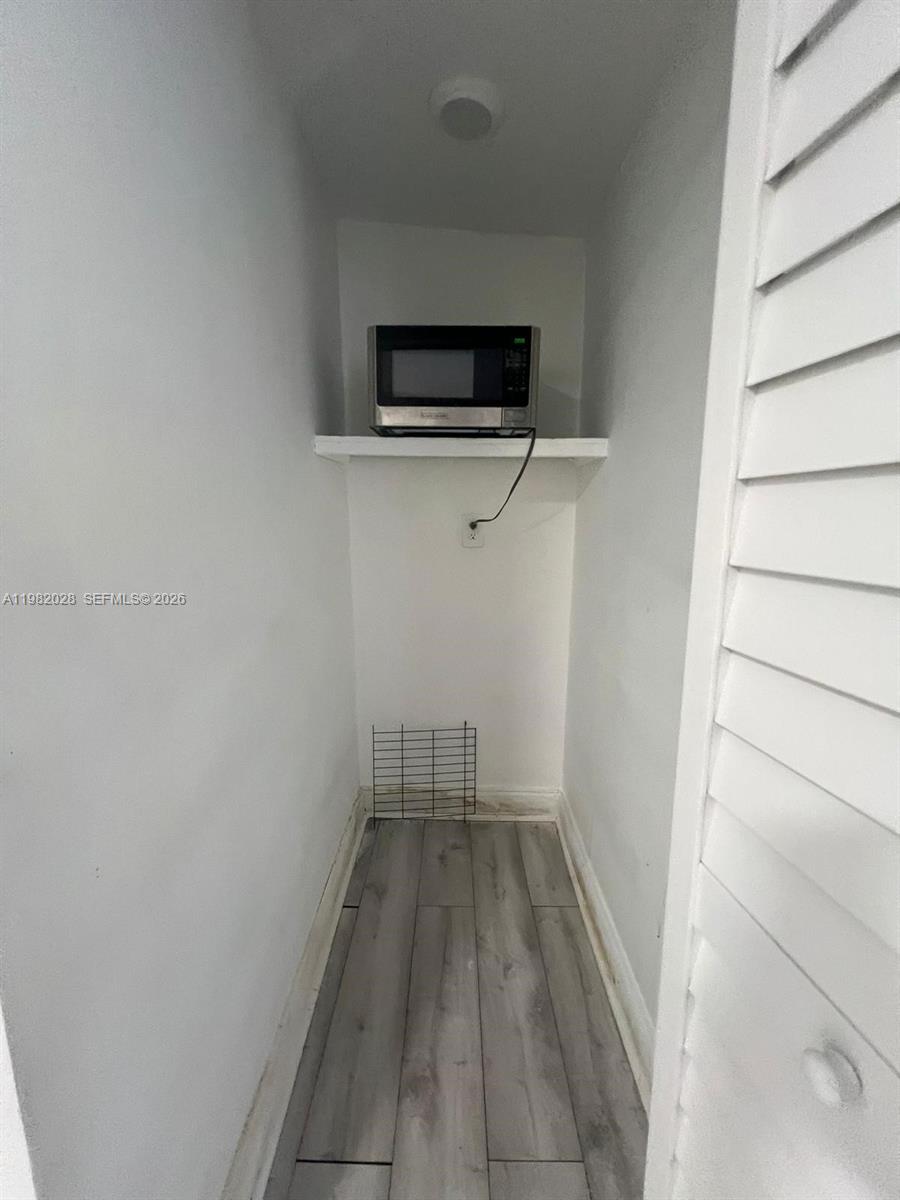 A small, narrow closet space features light wood-look flooring and a microwave on a shelf — 1053 NE 149th St, Miami FL 33161, MIAMI, FL
