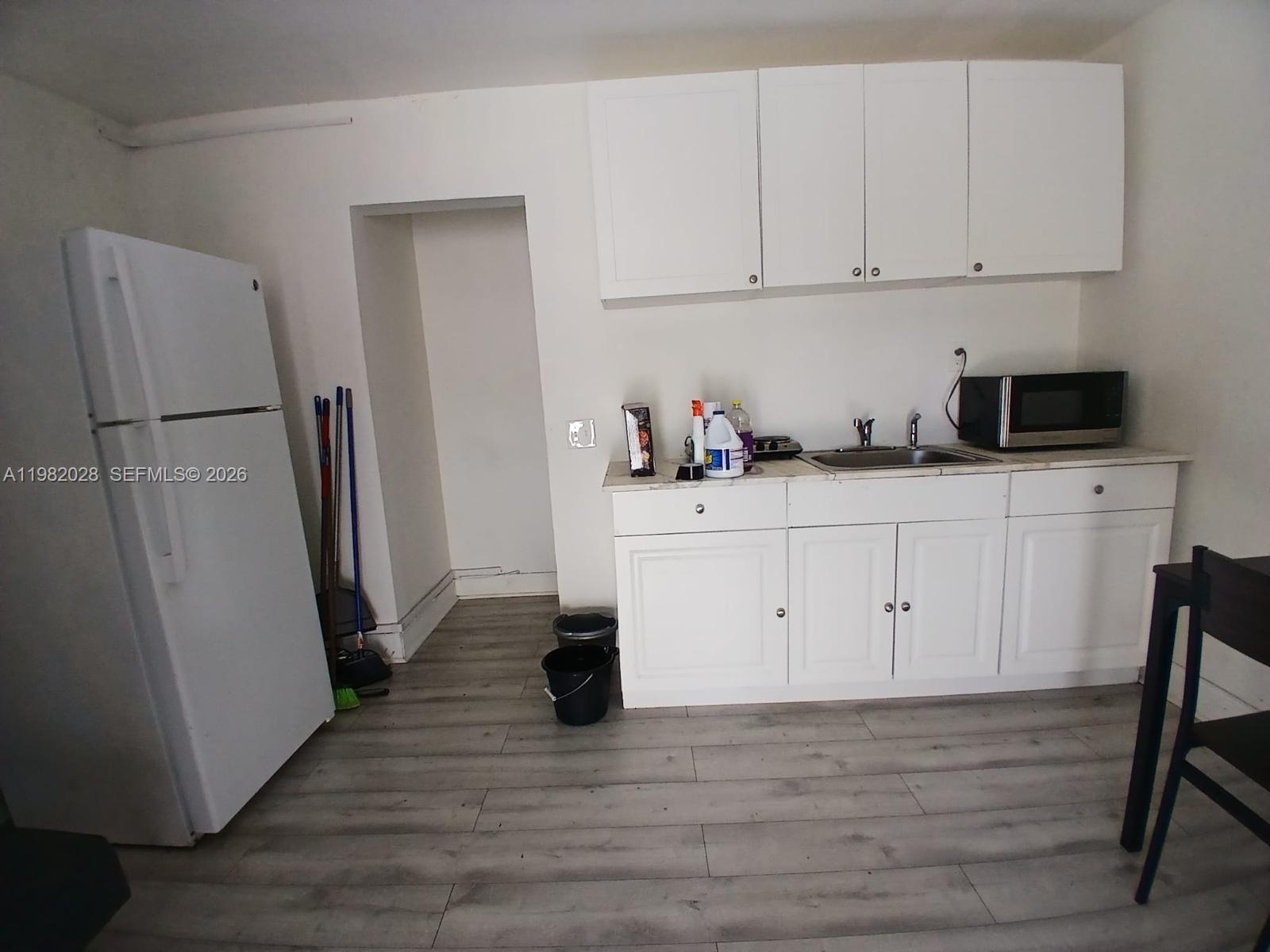 A kitchen features white cabinets, a refrigerator, a sink, and light wood-look flooring — 1053 NE 149th St, Miami FL 33161, MIAMI, FL