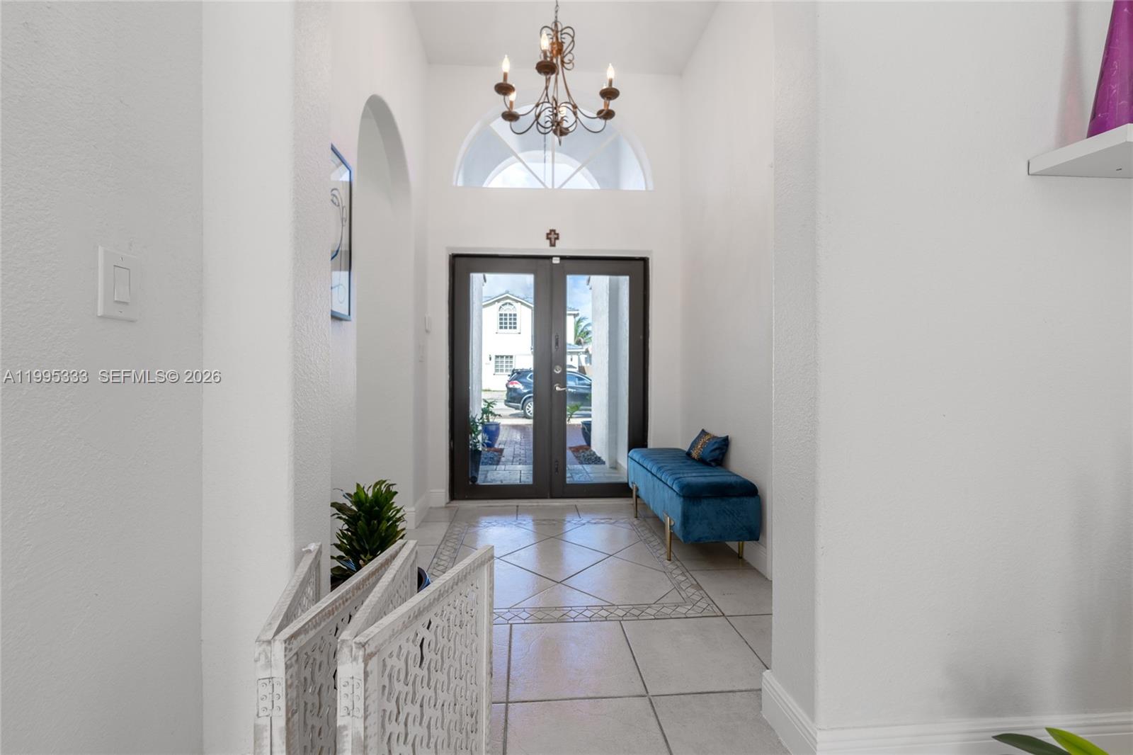 A bright entryway features a tiled floor, a blue velvet bench, and a chandelier — 3551 SW 152nd Pass, Miami FL 33185, MIAMI, FL