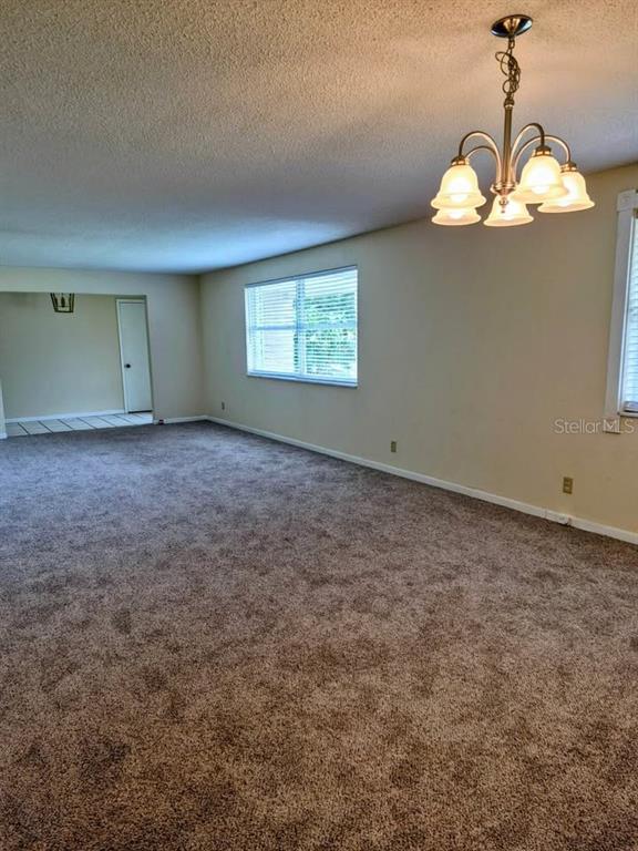An empty room features beige walls, brown carpeting, and a four-light chandelier — 39 PINE VALLEY CIRCLE, ORMOND BEACH, FL