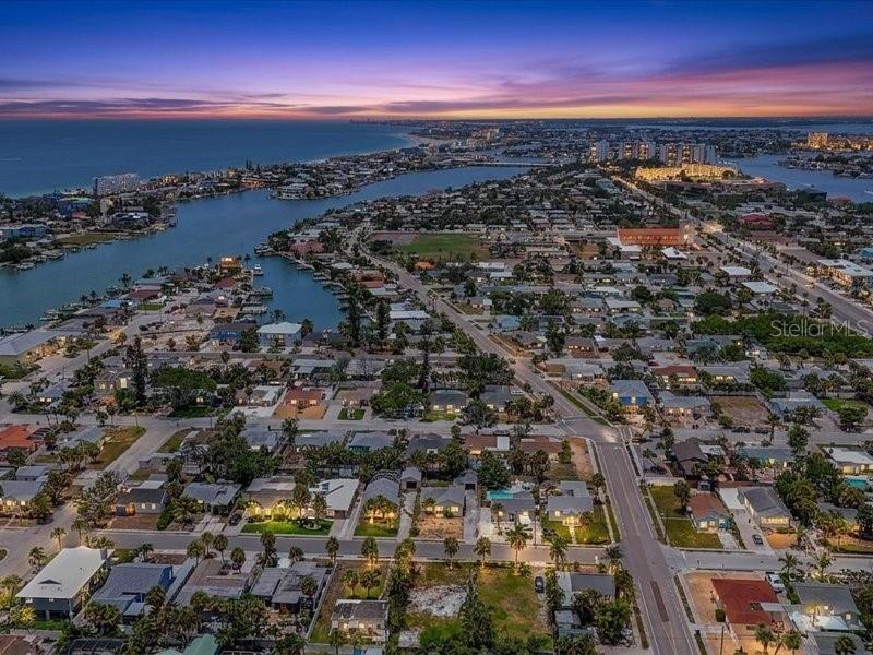 An aerial view shows a coastal residential neighborhood at sunset with a waterway nearby — 516 78TH AVENUE, ST PETE BEACH, FL