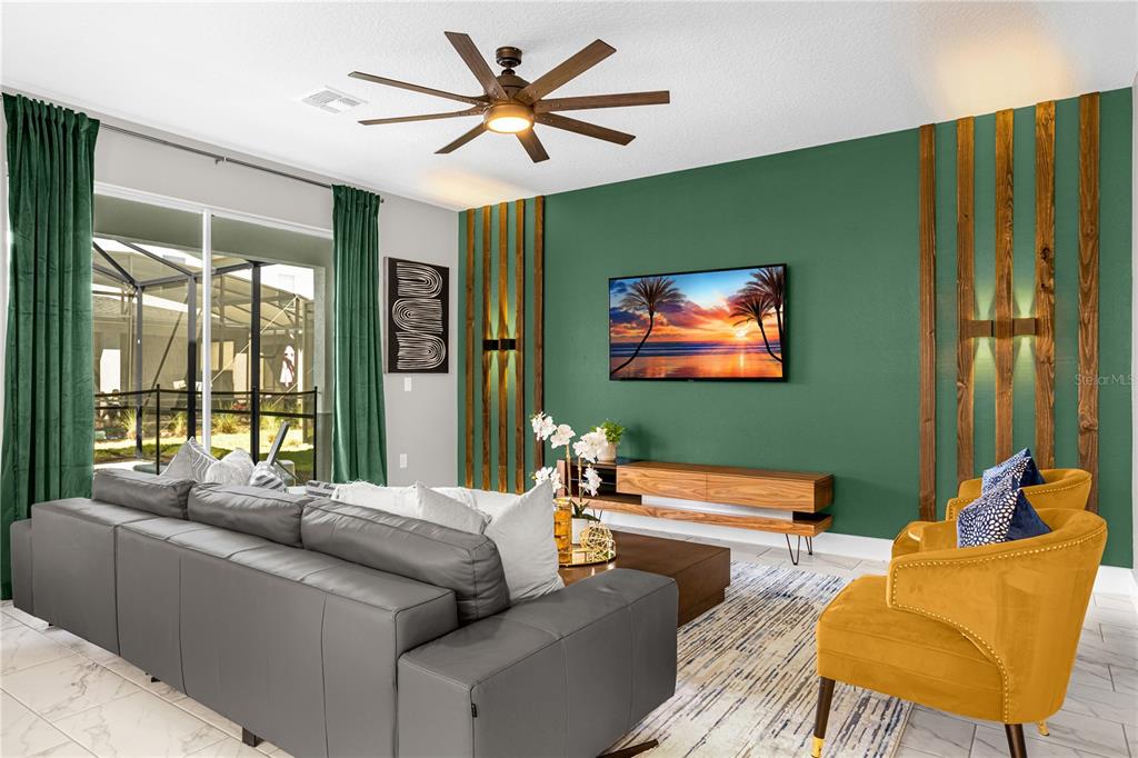 A living room features a green accent wall with wood slats, a gray sofa, and chairs — 2772 BOOKMARK DRIVE, KISSIMMEE, FL