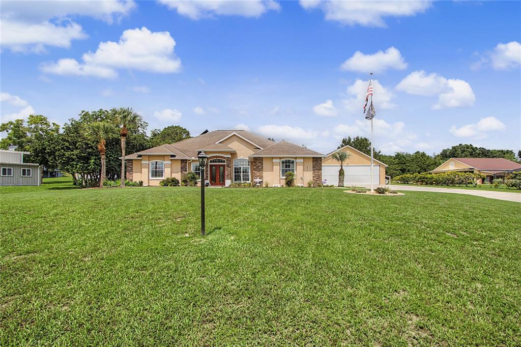 A single-story tan house with a stone facade, a large lawn, and a flagpole — 8840 SE 70 TERR, OCALA, FL