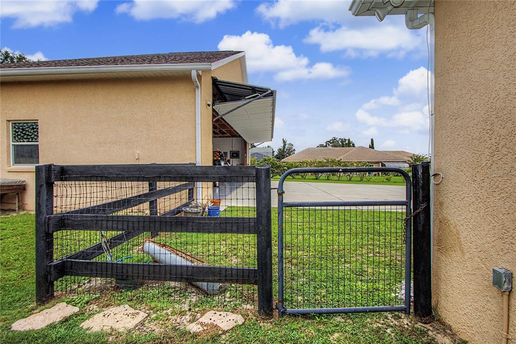 A black wooden fence and metal gate stand on a grassy lawn beside a house — 8840 SE 70 TERR, OCALA, FL