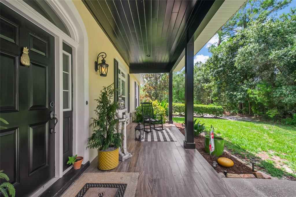 A covered front porch features wood-look tile flooring, a black door, and a rocking chair — 450 VALLEY STREAM DRIVE, GENEVA, FL