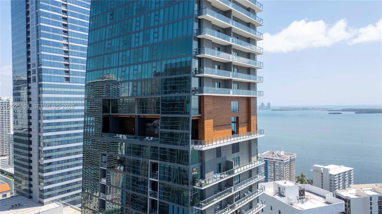 An exterior view of a modern glass high-rise building featuring a large open-air terrace — 1451 Brickell Ave # 2606, Miami FL 33131, MIAMI, FL