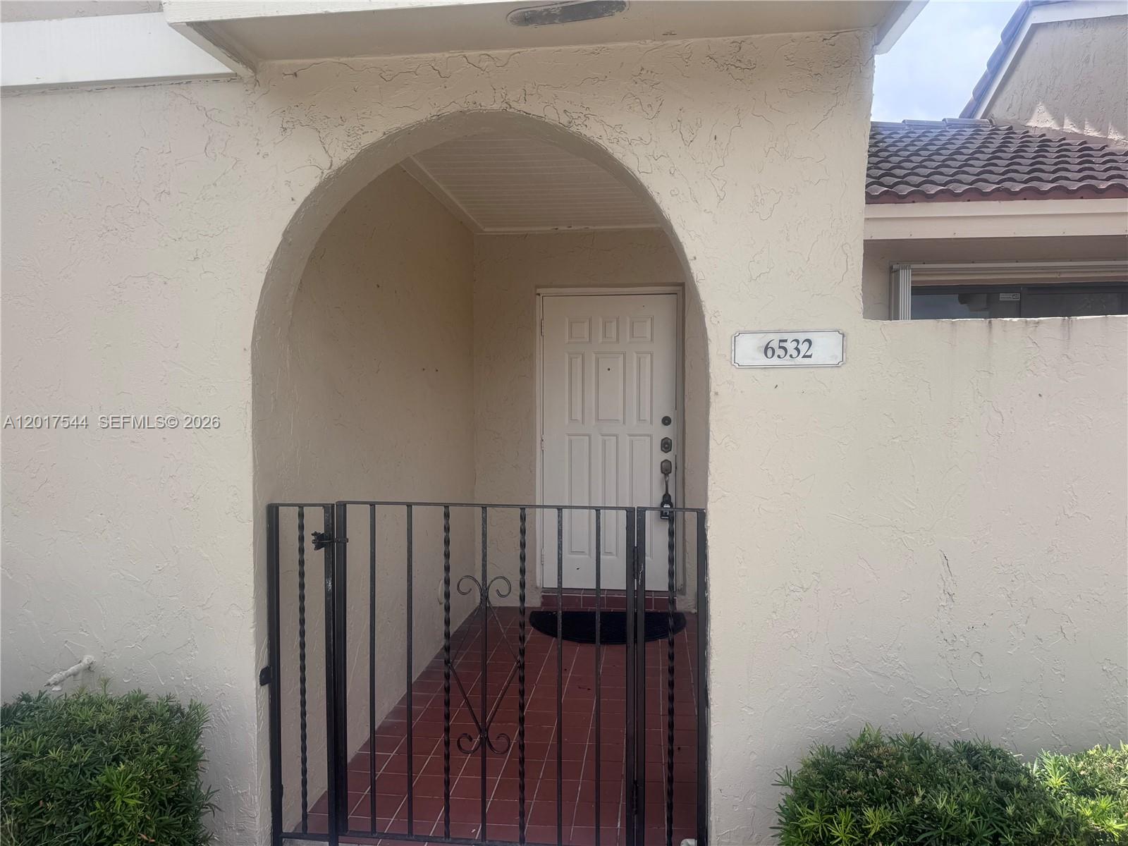 The exterior of a tan stucco townhouse features an arched entryway with a metal gate — 6532 NW 170th Ter, Hialeah FL 33015, HIALEAH, FL