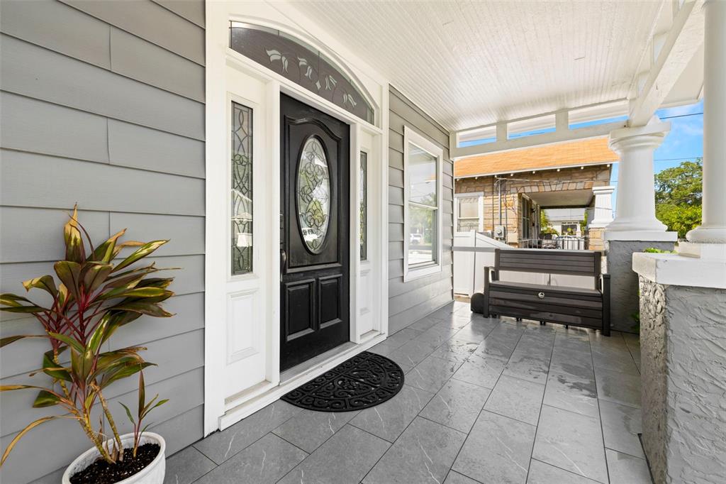 A covered front porch features gray tile flooring, a black front door, and a bench — 2526 W UNION STREET, TAMPA, FL