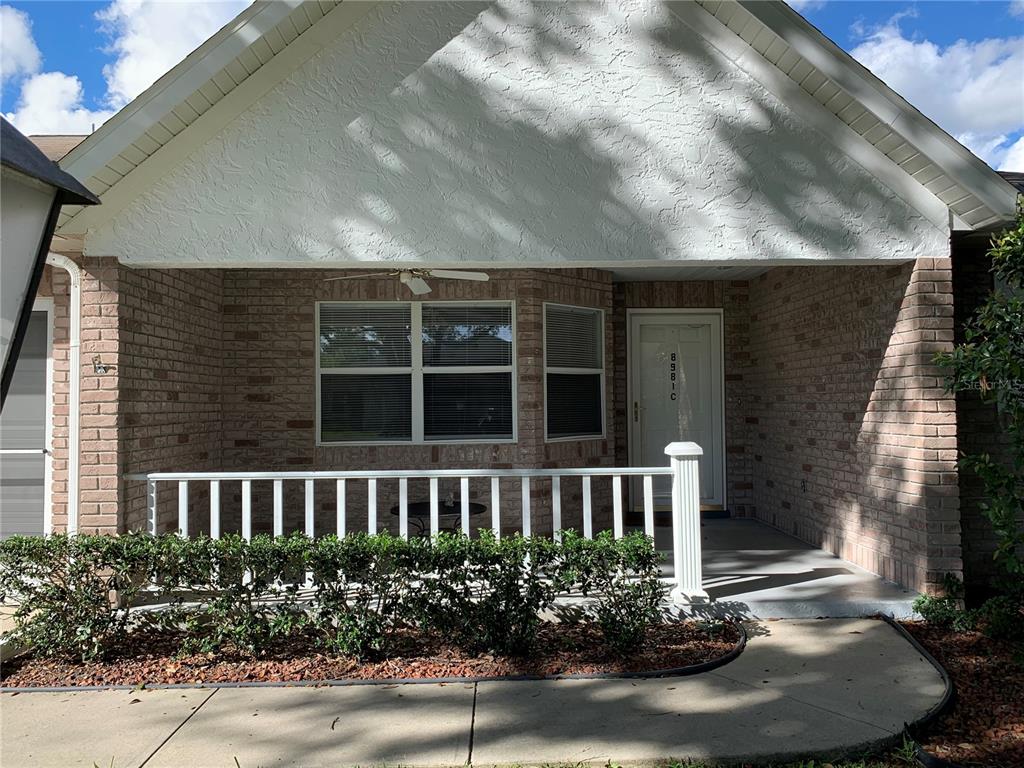 A brick house exterior features a covered front porch with a white railing and landscaping — 8981 SW 95TH STREET UNIT C, OCALA, FL