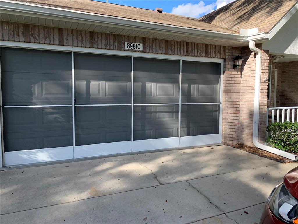 A garage exterior features a white sliding screen door system installed over the garage opening — 8981 SW 95TH STREET UNIT C, OCALA, FL
