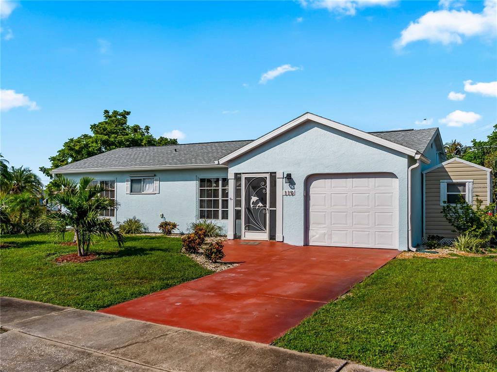 A light blue, single-story house features a red concrete driveway and a white garage door — 119 OLDENBURGH COURT NE, PORT CHARLOTTE, FL