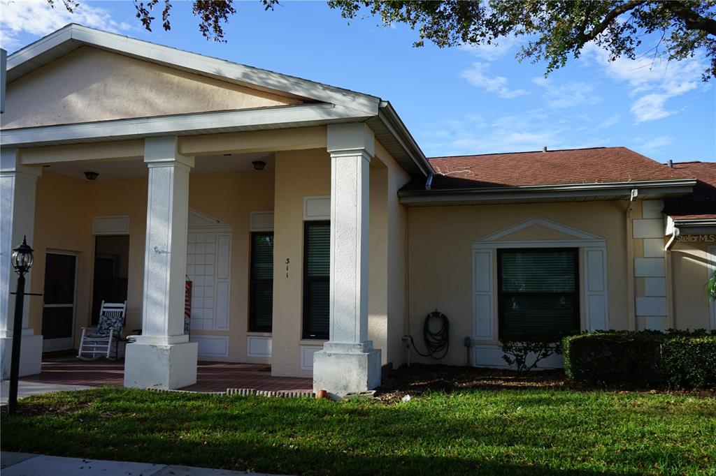 A covered porch with red tile flooring leads to a light-colored front door — 311 KELSEY WAY UNIT 3, SUN CITY CENTER, FL