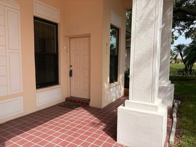 A hallway with tile flooring leads to a window with patterned curtains and a kitchen counter — 311 KELSEY WAY UNIT 3, SUN CITY CENTER, FL
