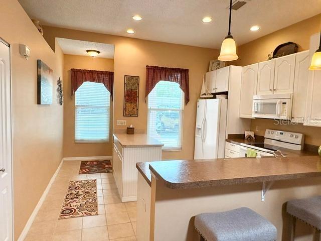 A kitchen with white cabinets and a breakfast bar overlooks a living area with flooring — 311 KELSEY WAY UNIT 3, SUN CITY CENTER, FL