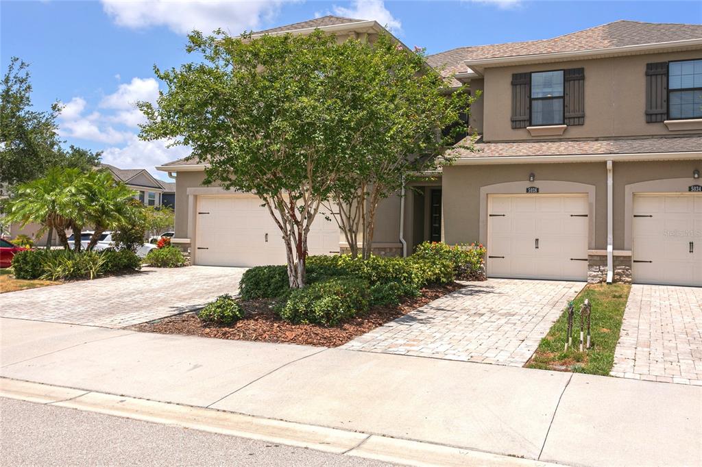 A two-story townhouse exterior features two garage doors, a paved driveway, and a small tree — 5038 SUNNYSIDE LANE, BRADENTON, FL