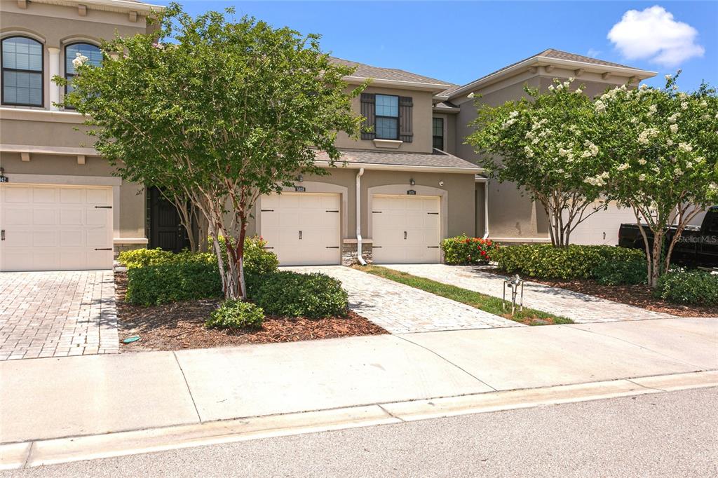 A row of two-story townhomes features beige stucco exteriors, arched garage doors, and paved driveways — 5038 SUNNYSIDE LANE, BRADENTON, FL