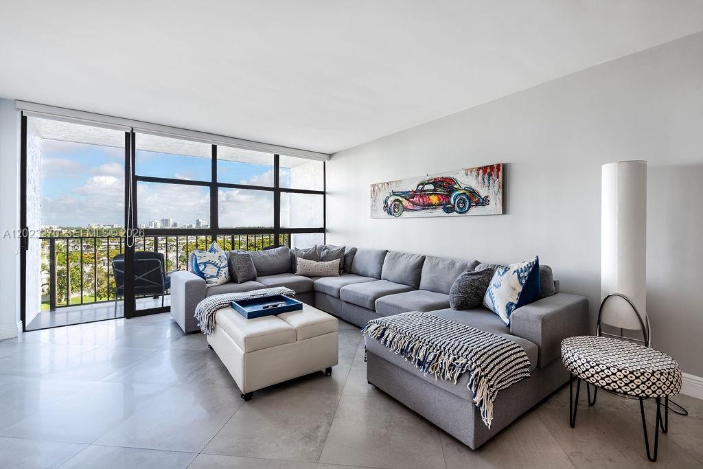 A living room features a gray sectional sofa, a white ottoman, and floor-to-ceiling windows — 600 Parkview Dr # 829, Hallandale Beach FL 33009, HALLANDALE BEACH, FL