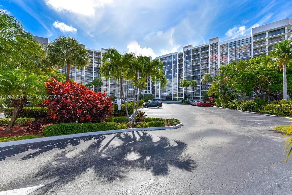 A multi-story apartment building stands behind a parking lot with palm trees and landscaping — 600 Parkview Dr # 829, Hallandale Beach FL 33009, HALLANDALE BEACH, FL