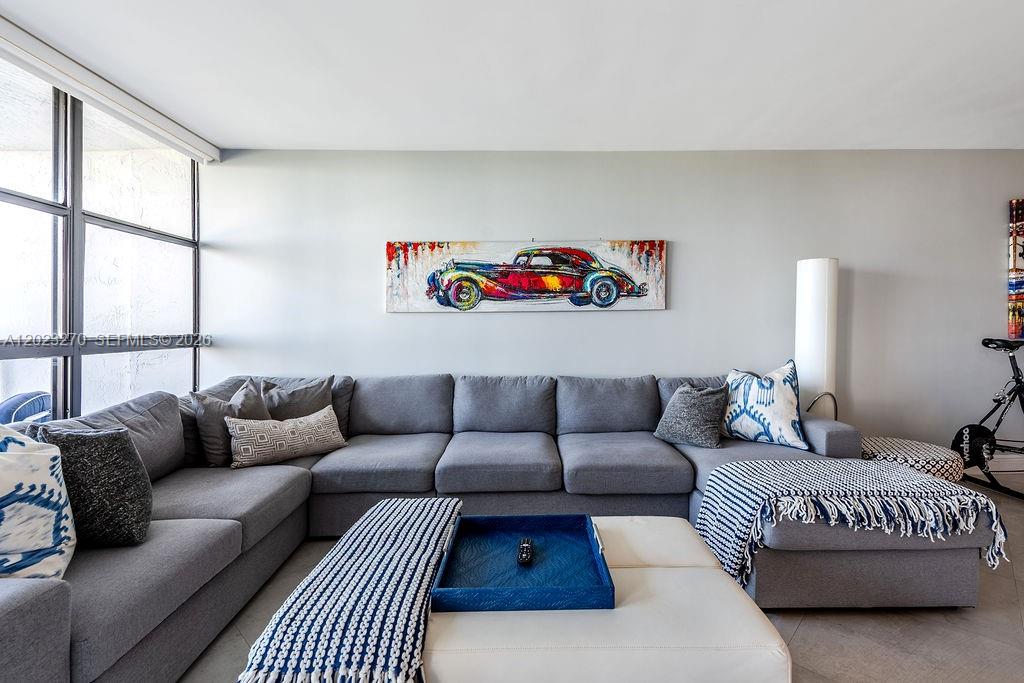 A living room features a large gray sectional sofa, a white ottoman, and wall art — 600 Parkview Dr # 829, Hallandale Beach FL 33009, HALLANDALE BEACH, FL