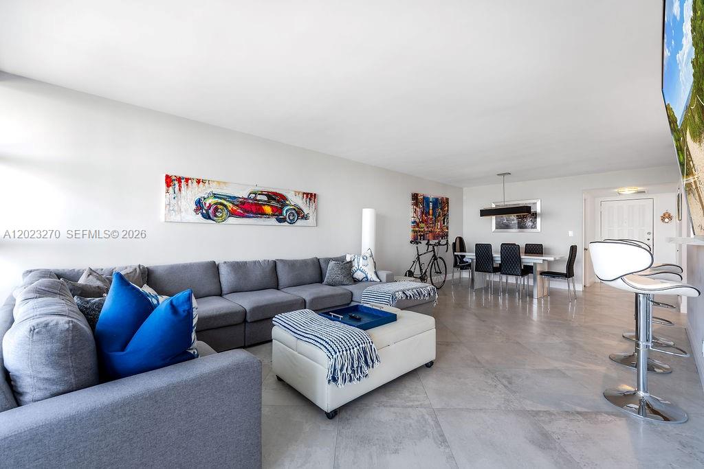 A modern living room features a gray sectional sofa, a white ottoman, and dining area — 600 Parkview Dr # 829, Hallandale Beach FL 33009, HALLANDALE BEACH, FL
