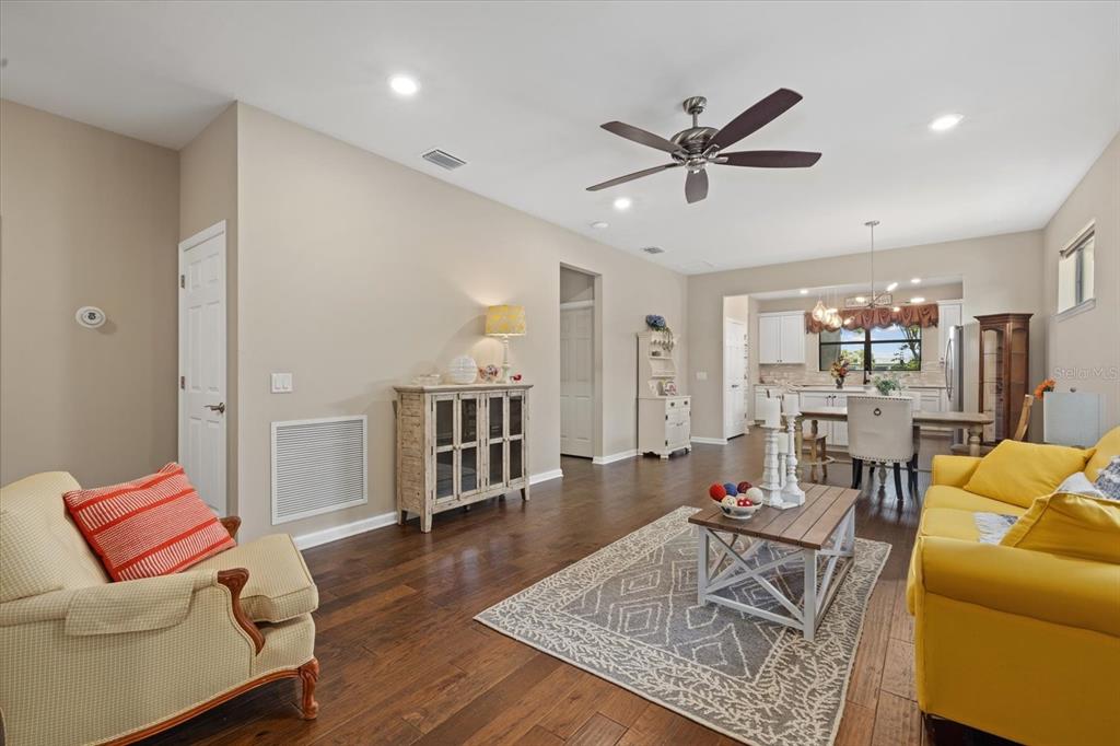 A living room with hardwood floors, a ceiling fan, and an open kitchen area — 17011 HAMPTON FALLS TERRACE, LAKEWOOD RANCH, FL