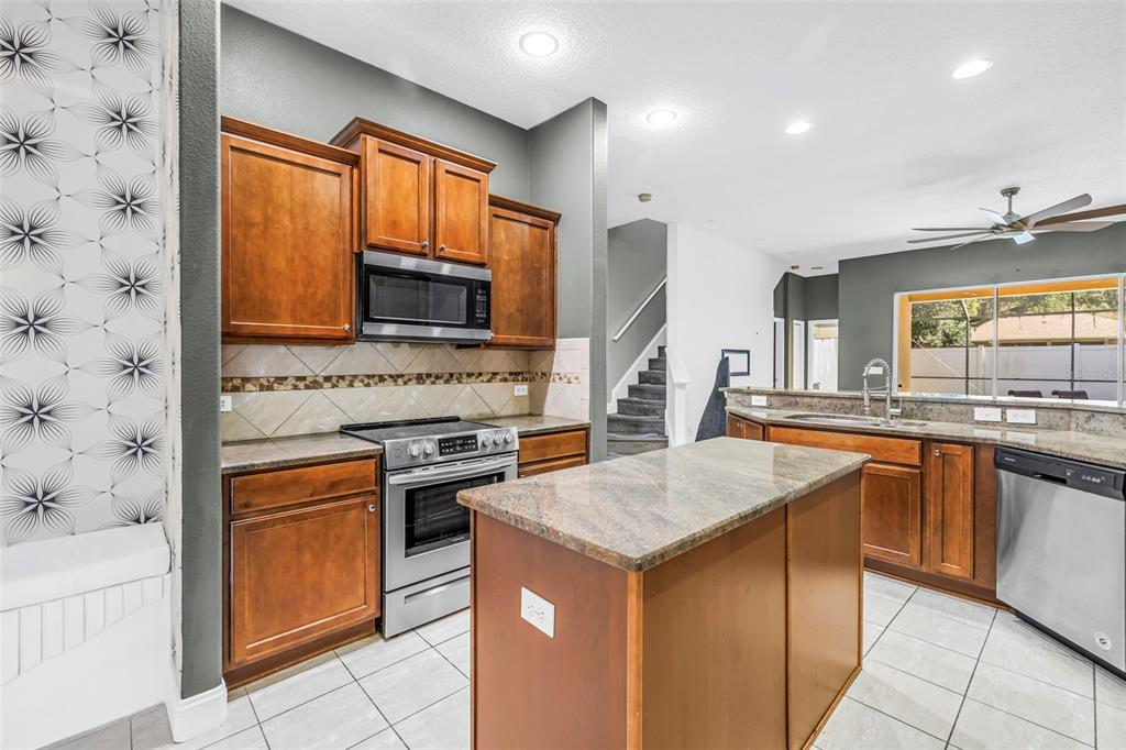A kitchen with wood cabinets, granite countertops, and a stainless steel dishwasher overlooks a pool — 27405 SORA BOULEVARD, WESLEY CHAPEL, FL