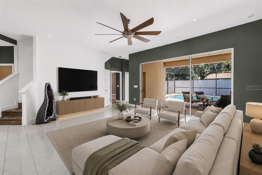 A modern living room features a large sectional, a circular coffee table, and pool views — 27405 SORA BOULEVARD, WESLEY CHAPEL, FL