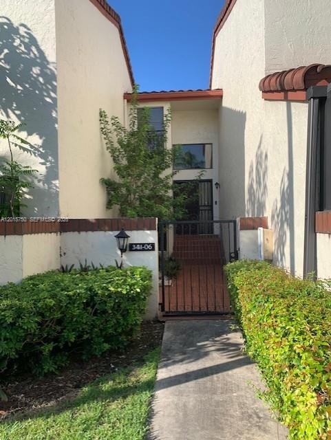 A concrete walkway leads to the gated entrance of a two-story stucco townhouse — 341 Ives Dairy Rd # 06, Miami FL 33179, MIAMI, FL