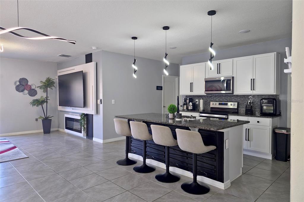 A modern kitchen features white cabinets, a dark island with bar stools, and tiled flooring — 1292 CASCADES AVENUE, DAVENPORT, FL