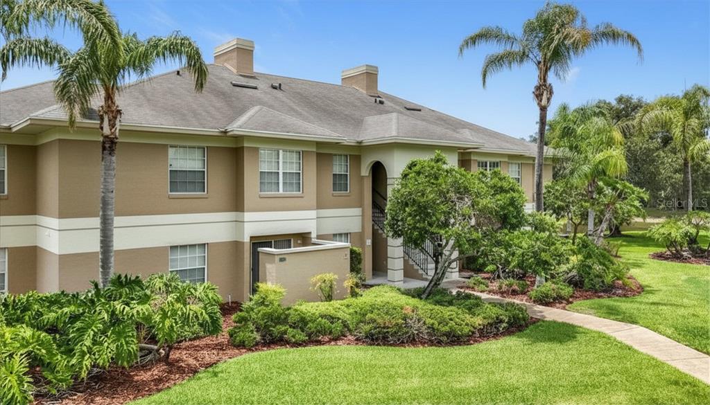 A two-story apartment building with beige stucco siding, a shingled roof, and landscaped grounds — 704 EAGLE POND DRIVE UNIT 704, WINTER HAVEN, FL
