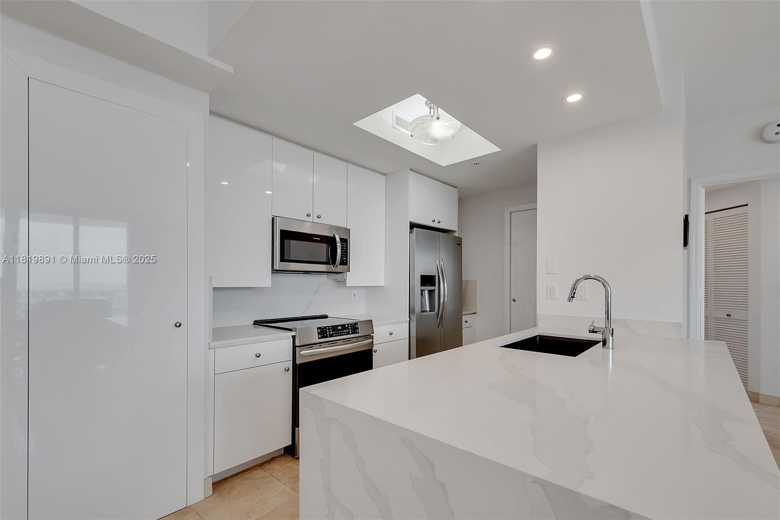 A modern kitchen features white cabinets, stainless steel appliances, and a white marble-patterned island — 848 Brickell Key Dr # 1803, Miami FL 33131, MIAMI, FL