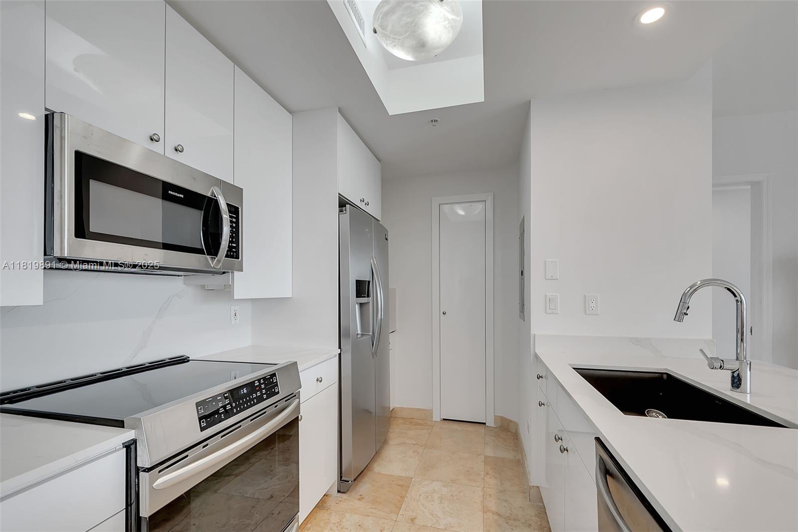 A modern kitchen features white cabinets, stainless steel appliances, and a light-colored stone floor — 848 Brickell Key Dr # 1803, Miami FL 33131, MIAMI, FL