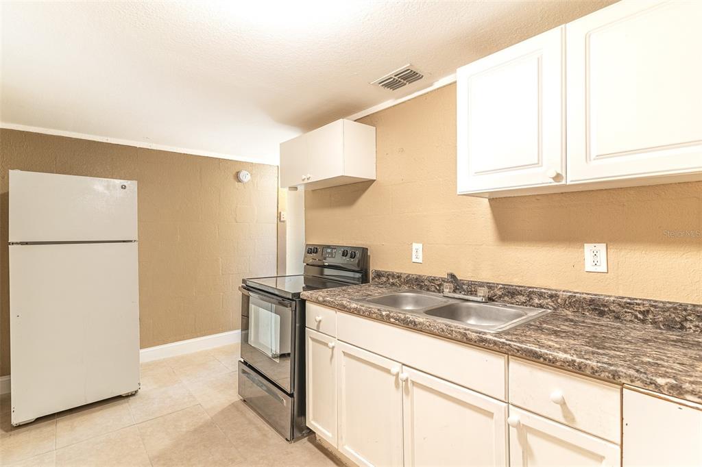 A kitchen with white cabinets, a stainless steel stove, a white refrigerator, and brown walls — 114 E NORTHSIDE DRIVE UNIT 3, LAKE WALES, FL