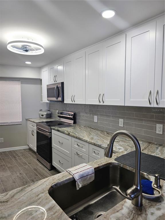 A kitchen features white cabinets, granite countertops, a stainless steel stove, and a gray backsplash — 3100 GULF BOULEVARD UNIT 221, BELLEAIR BEACH, FL