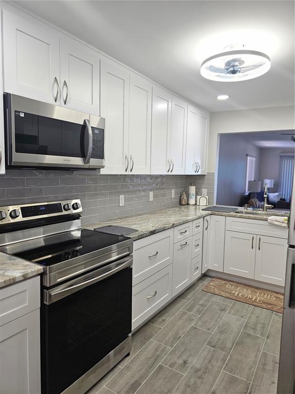 A kitchen features white cabinets, stainless steel appliances, granite countertops, and gray tile flooring — 3100 GULF BOULEVARD UNIT 221, BELLEAIR BEACH, FL