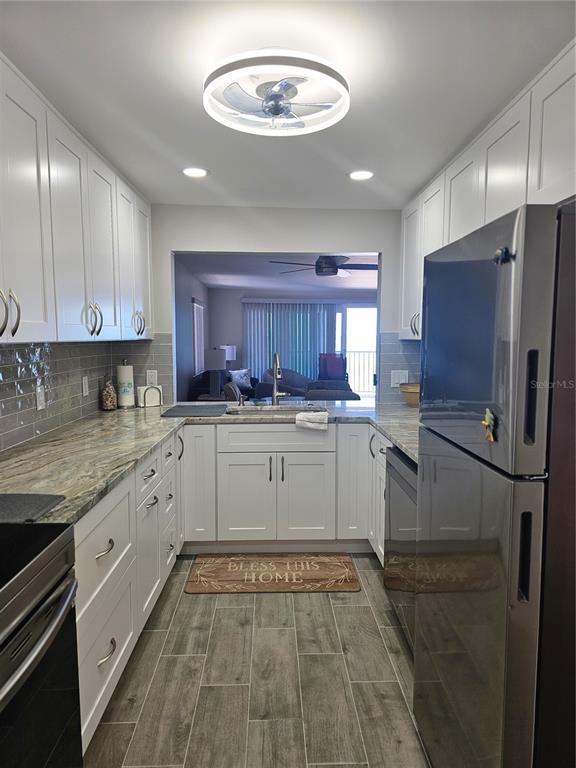 A galley kitchen features white cabinets, granite countertops, stainless steel appliances, and wood-look tile flooring — 3100 GULF BOULEVARD UNIT 221, BELLEAIR BEACH, FL