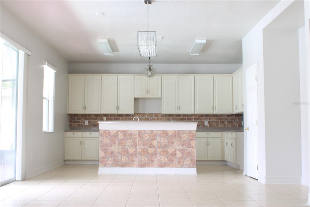 A kitchen features cream-colored cabinets, a tiled island, and a brick-patterned backsplash — 1338 BLACKWATER POND DRIVE, ORLANDO, FL