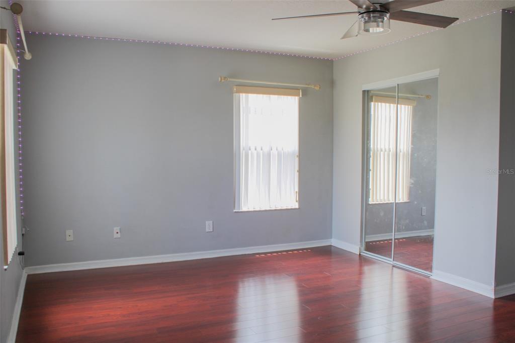 An empty bedroom features gray walls, dark wood flooring, a ceiling fan, and mirrored closet doors — 1338 BLACKWATER POND DRIVE, ORLANDO, FL