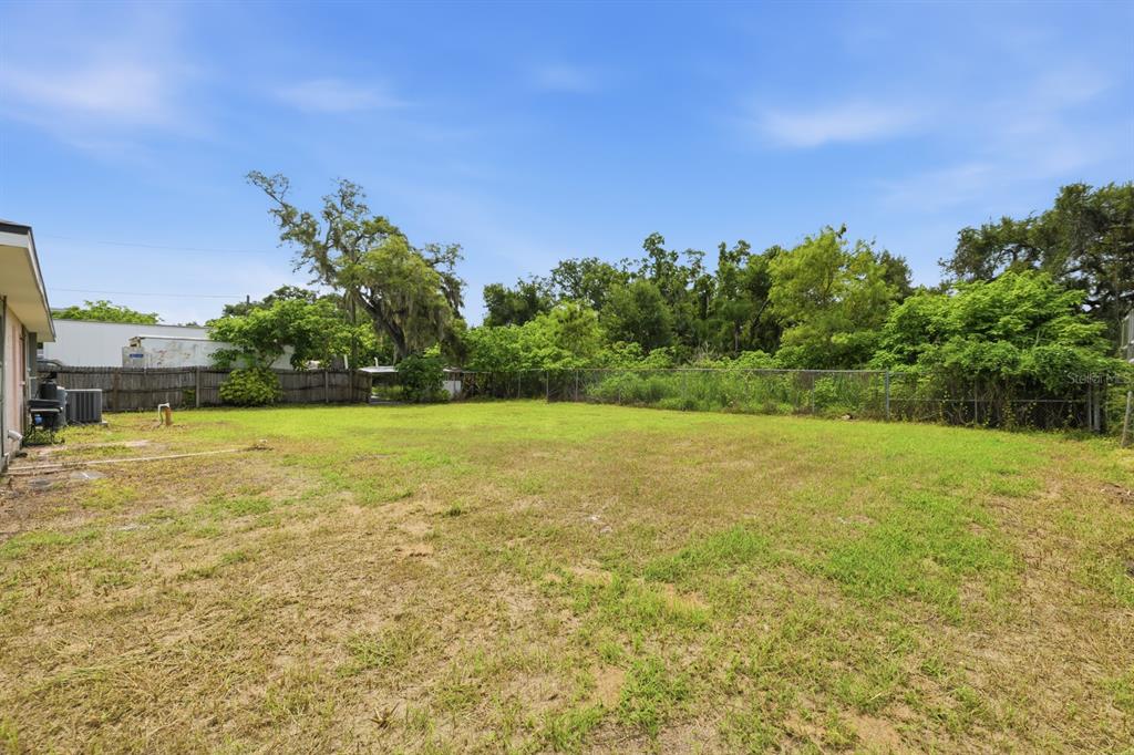 A large, grassy backyard features a chain-link fence and mature trees under a blue sky — 7113 CAUSEWAY BOULEVARD, TAMPA, FL
