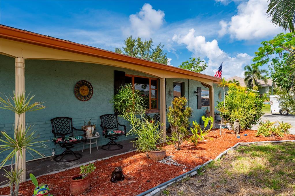 A teal house exterior features a covered porch with two chairs and red mulch landscaping — 611 BONITA COURT, PUNTA GORDA, FL