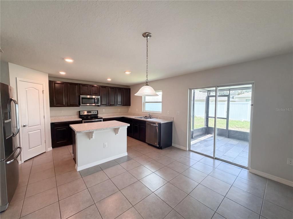 A kitchen features dark wood cabinets, a central island, stainless steel appliances, and tile flooring — 4272 MOON SHADOW LOOP, MULBERRY, FL